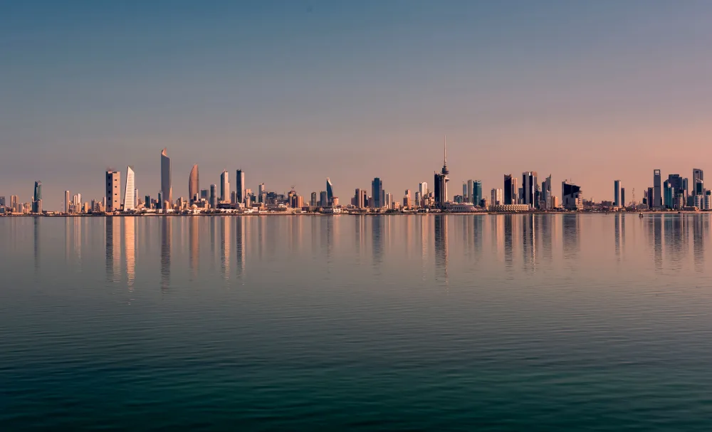 Kuwait City's skyline reflected in calm water at sunset