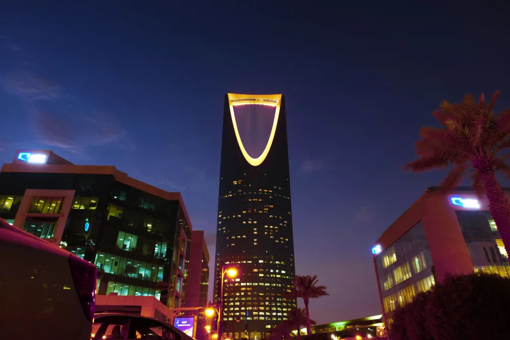 The Kingdom Centre tower illuminated at night among office buildings and palm trees in Riyadh, Saudi Arabia